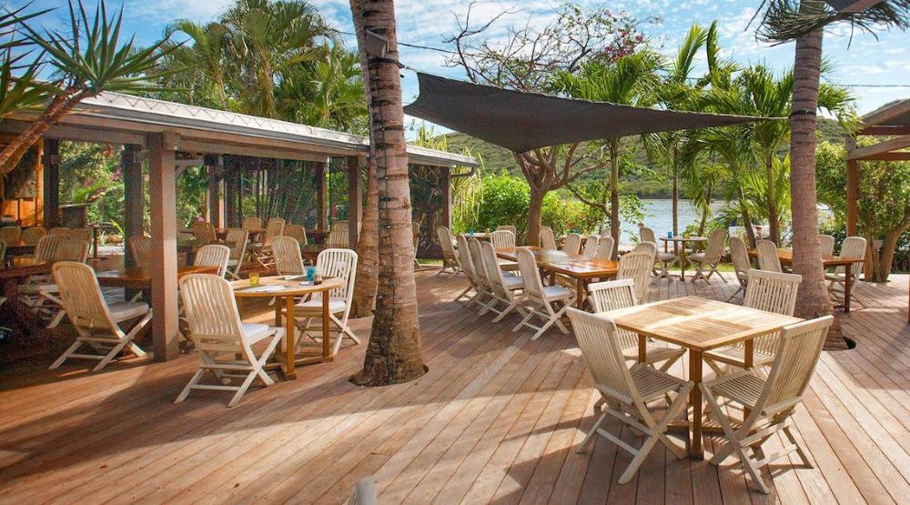 One of the most beautiful restaurants on Saint Barthélemy, featuring a sunny terrace with charming wooden tables and chairs, surrounded by tropical foliage and trees. 