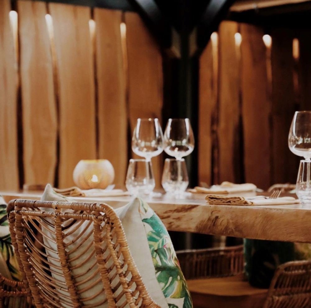 Discover some of the best restaurants on and around St. Barts in the Caribbean, one of which is pictured, with wine glasses and gorgeous wooden chairs and place settings.