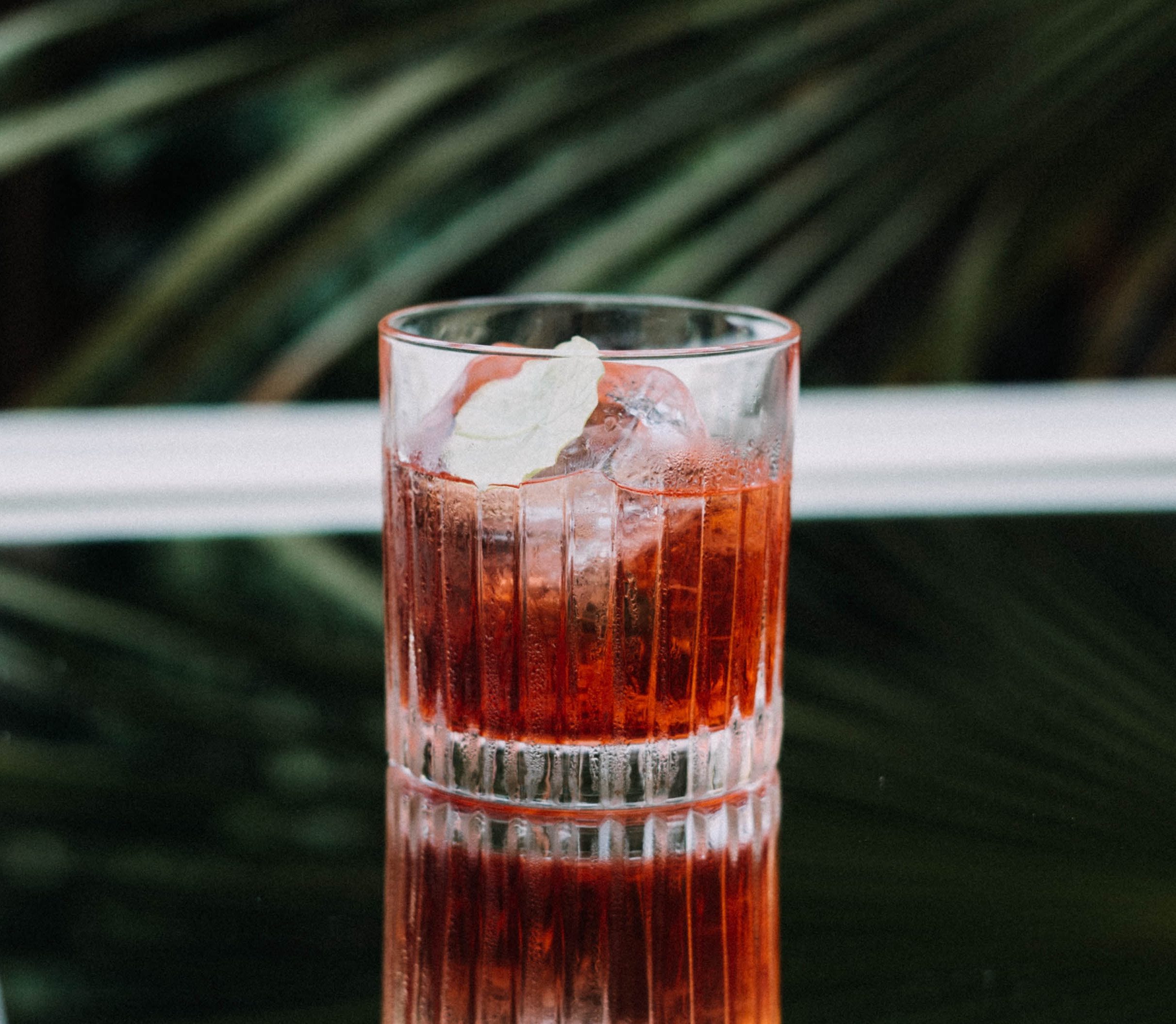 Another delicious Caribbean rum cocktail, the pictured cocktail is a spiced rum cocktail, an iced reddish brown drink on a mirrored table.