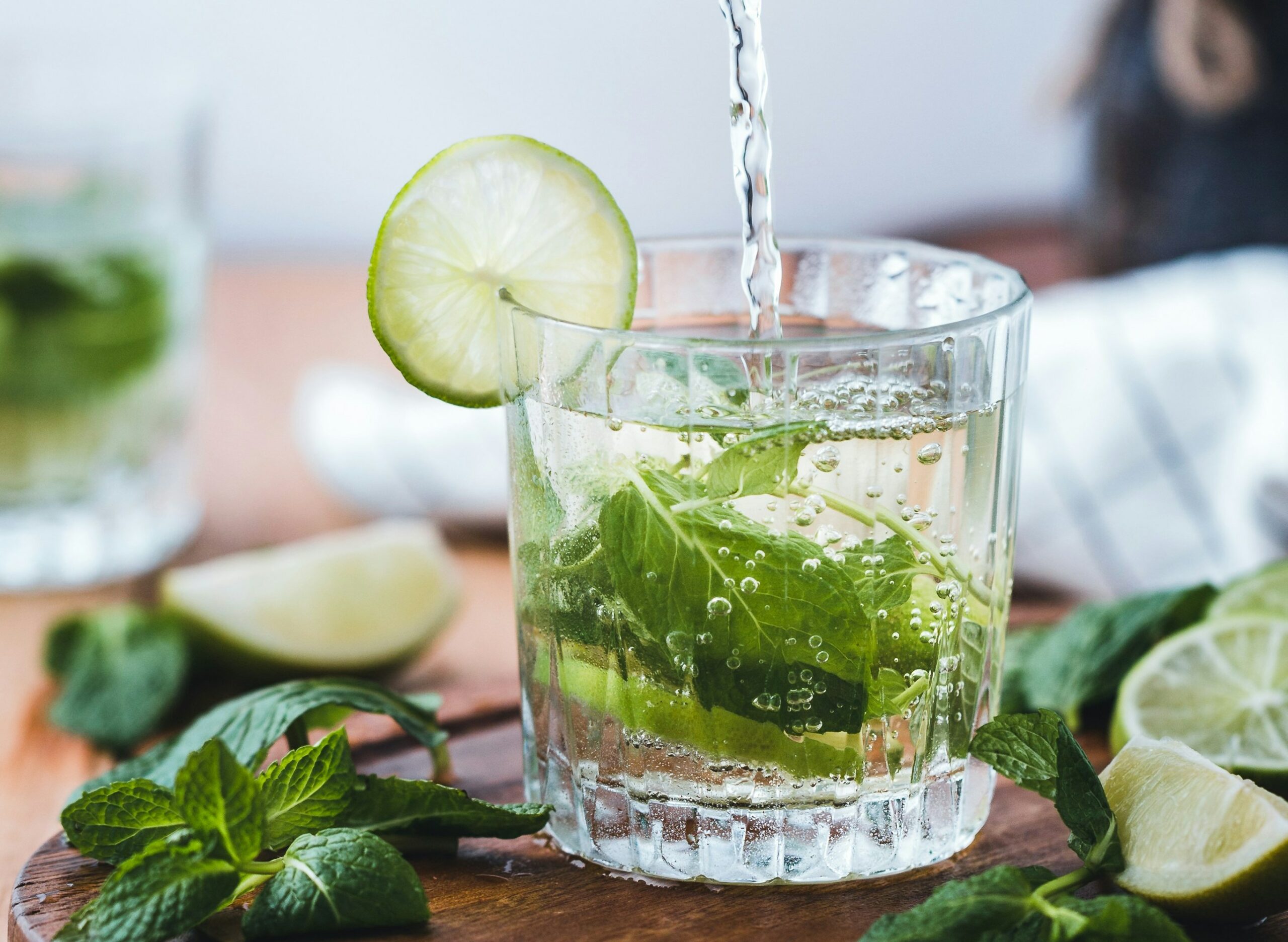 One of the best cocktails in the Caribbean and one of the most popular cocktails around the world, this is the classic mojito, a glass filled with clear liquid, lime juice, and mint leafs, with a round of lime as garnish on the rim.