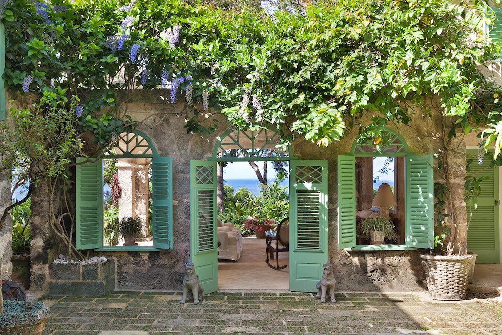 Gorgeous luxury villa in Barbados is perfect for honeymooners, looking quaint yet perfect similar to an Italian villa with leafy vines, teal trim, and open windows.