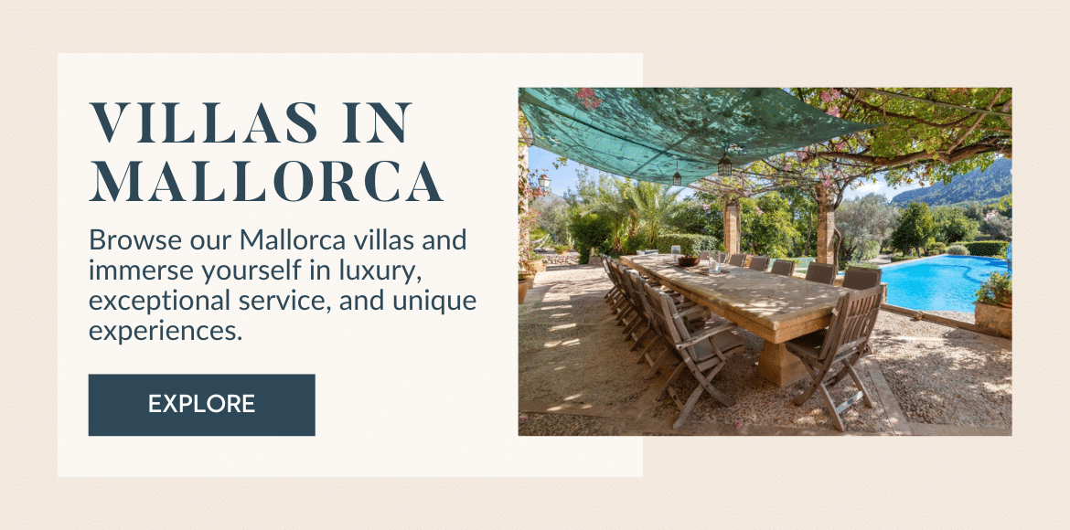 Outdoor dining area with a long wooden table and chairs under a leafy pergola beside a pool, surrounded by lush greenery and mountains, promoting luxury villas in Mallorca.