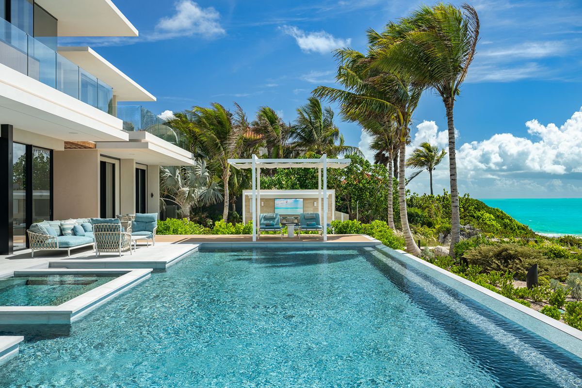 Modern villa with a swimming pool, lounge seating, and a poolside cabana overlooking the sea.